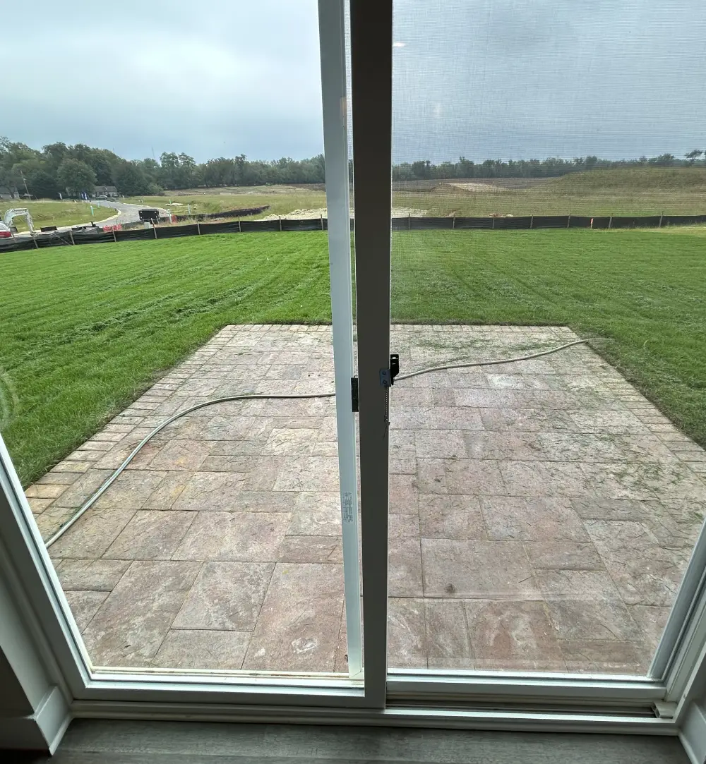 View of a green lawn and patio through a large glass door.